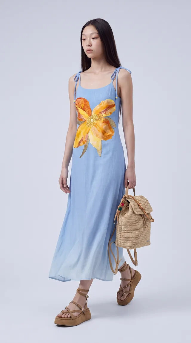 AI-generated still: a model standing in the flower dress with the sandals and backpack